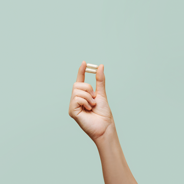 Hand holding two white prenatal vitamin capsules from the Complete Prenatal with Folate, DHA, and Choline.