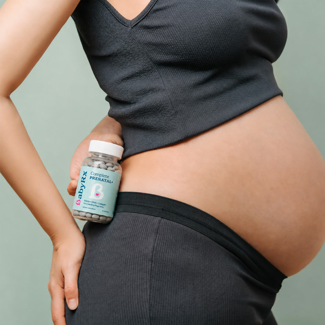 Pregnant person holding a bottle of BabyRx Complete Prenatal vitamins against a plain background